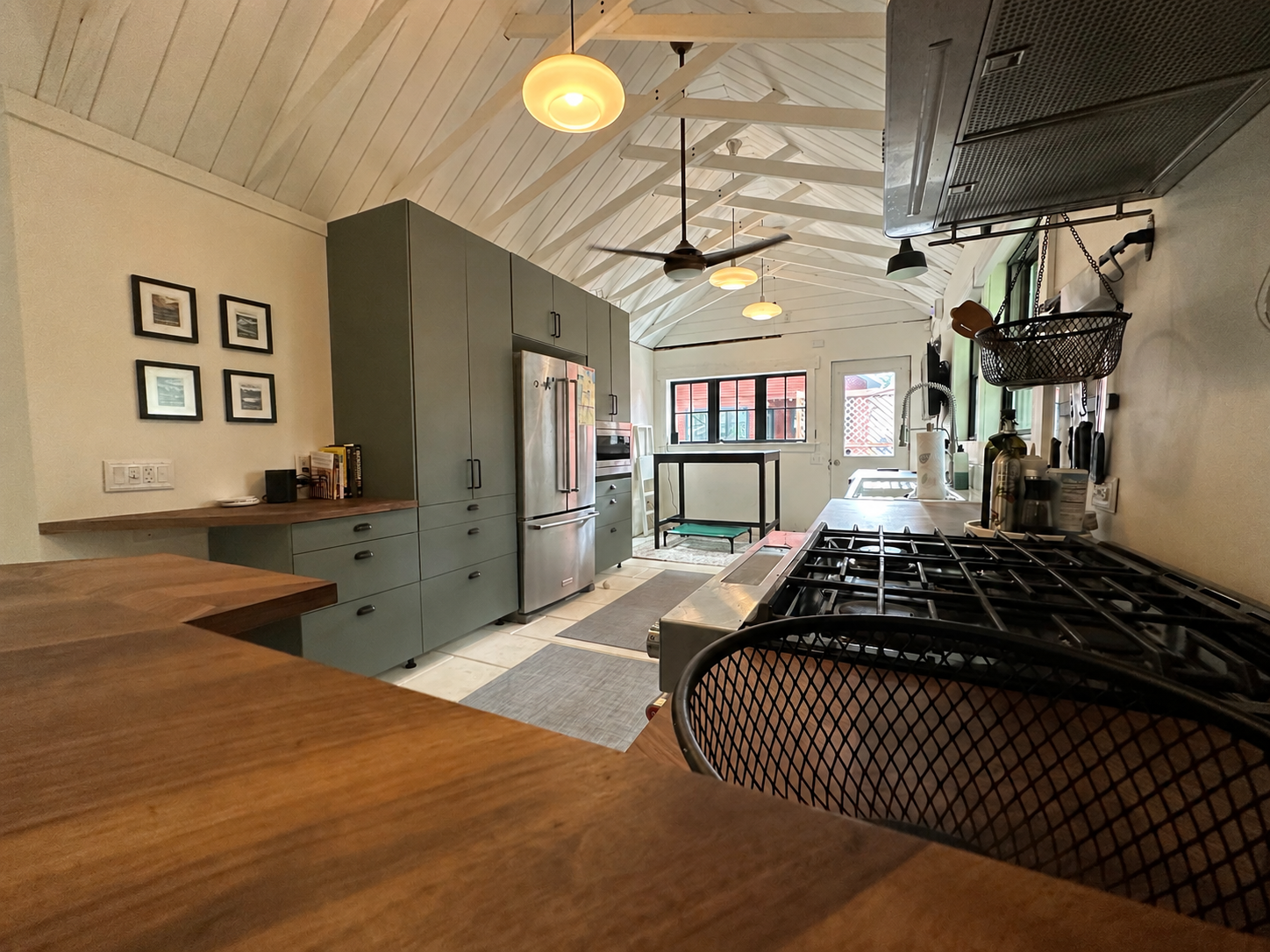 Kitchen with green cabinetry, butcher-block counters, stainless appliances, and a vaulted white ceiling